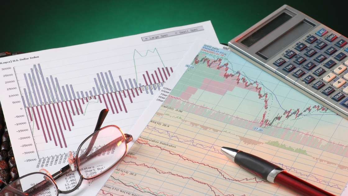 Two pages of graphs on a desk with glasses, a pen and a calculator on top of them